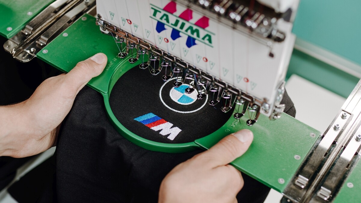 Nahaufnahme von einer Stickmaschine beim veredeln eines Logos auf schwarzem Polohemd