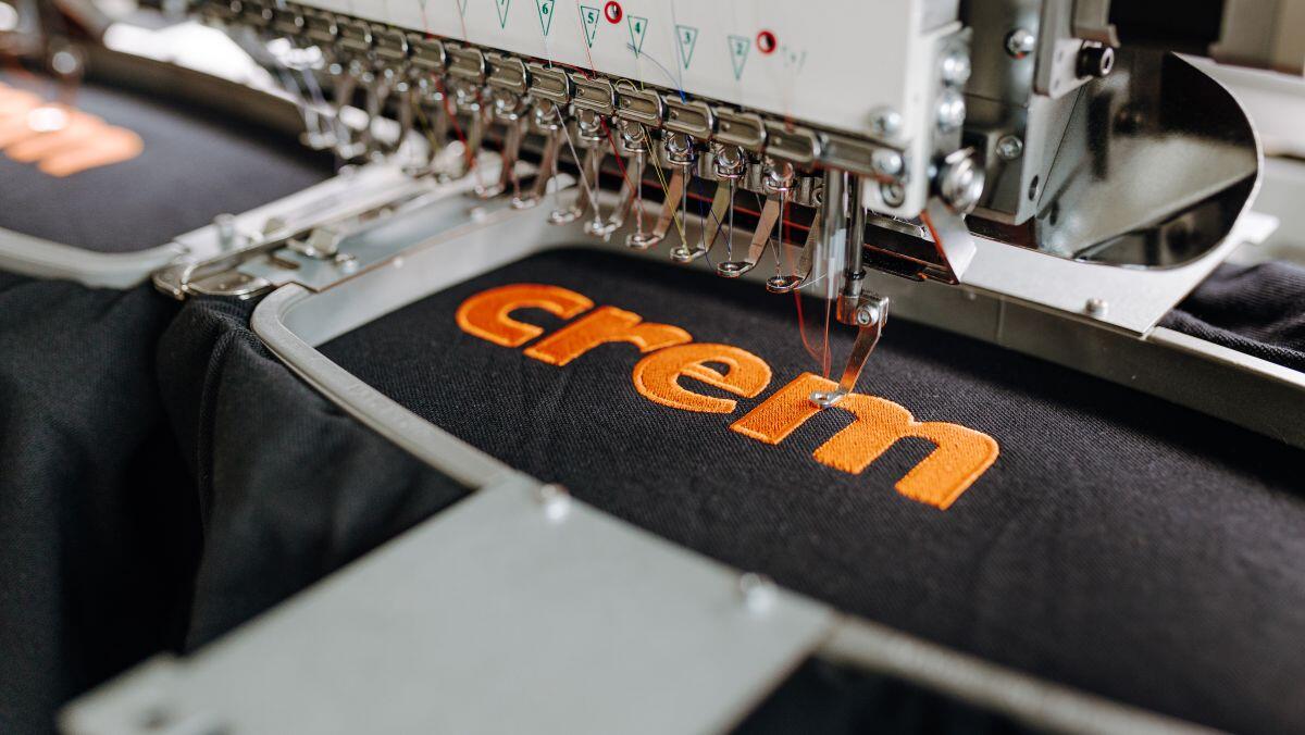 Nahaufnahme von einer Maschine beim besticken von einem Textil mit einem Logo