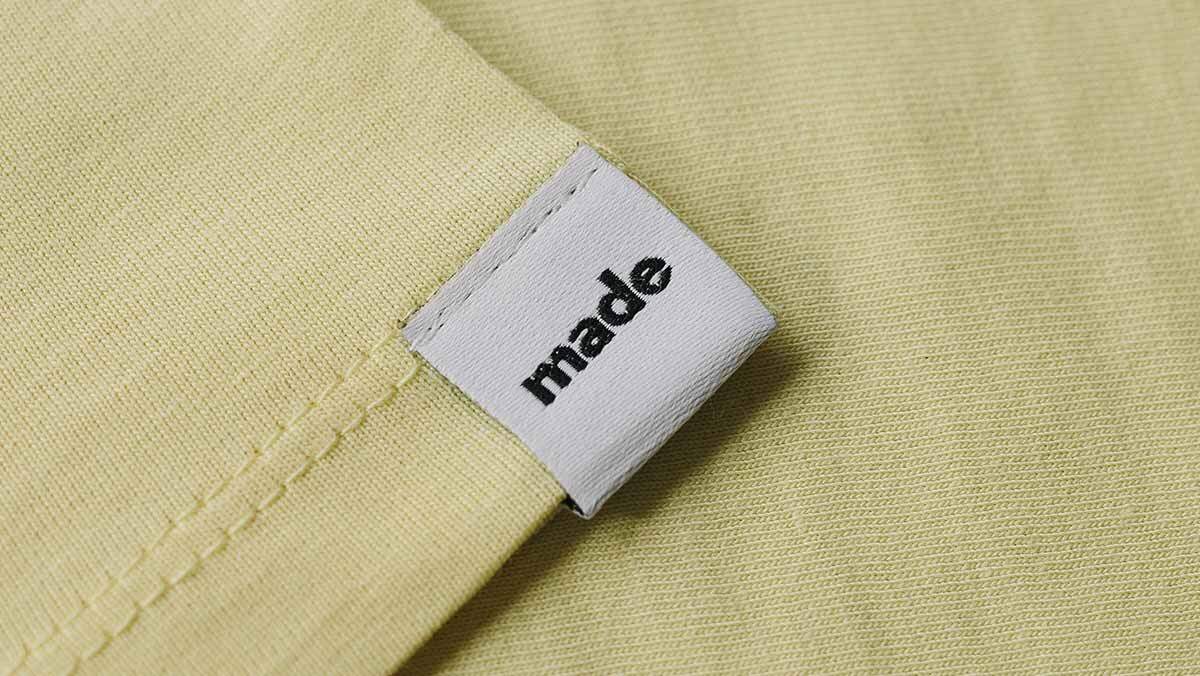 Eingewebte Motive Ein weißes Textiletikett mit einem schwarzen Logo auf einem gelben T-Shirt